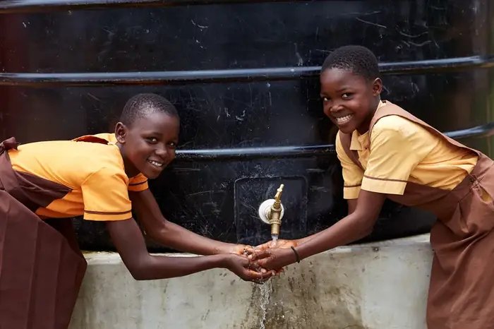 Two pupils washing their hands at a community water tank